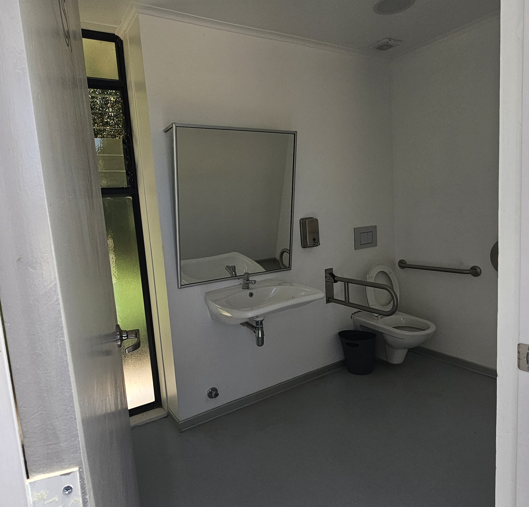 Fotografía del baño accesible, cuenta con un gran espejo, lavamanos accesible, barras de sugeción y sanitario